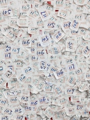 A large collection of visitor badges with handwritten numbers scattered chaotically. The numbers are mainly in blue ink, and the badges are made of paper with both English and Chinese text printed in red and blue. The background is mostly paper, displaying a dense and overlapping pattern due to the number of badges.