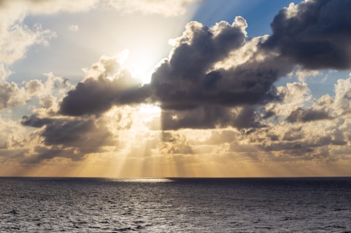 Sunlight breaking through thick clouds over a calm sea horizon.