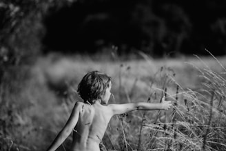 greyscale photography of child trying to hold plant