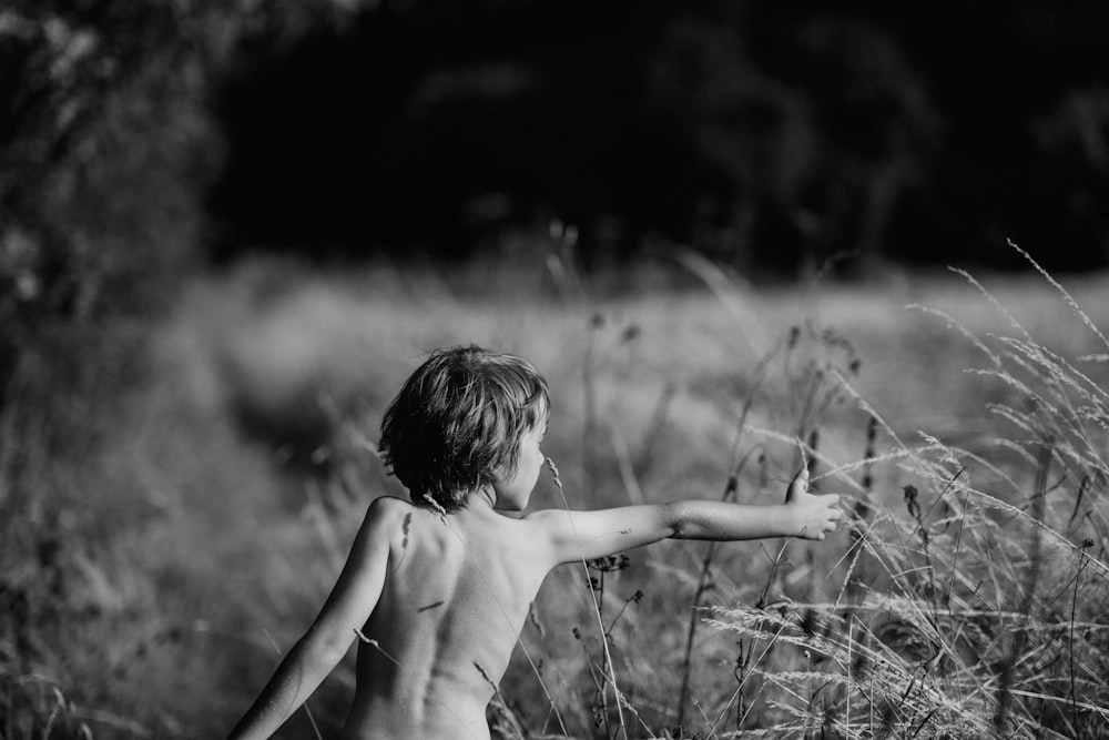 greyscale photography of child trying to hold plant