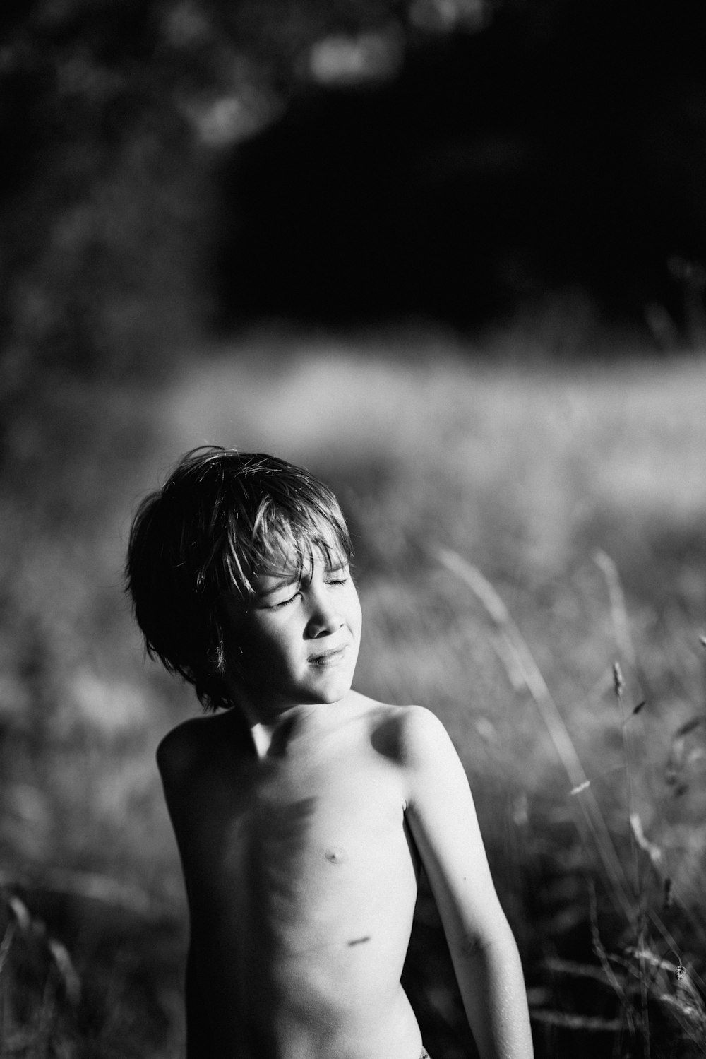 Graustufenfotografie eines Oben-ohne-Jungen neben Gräsern