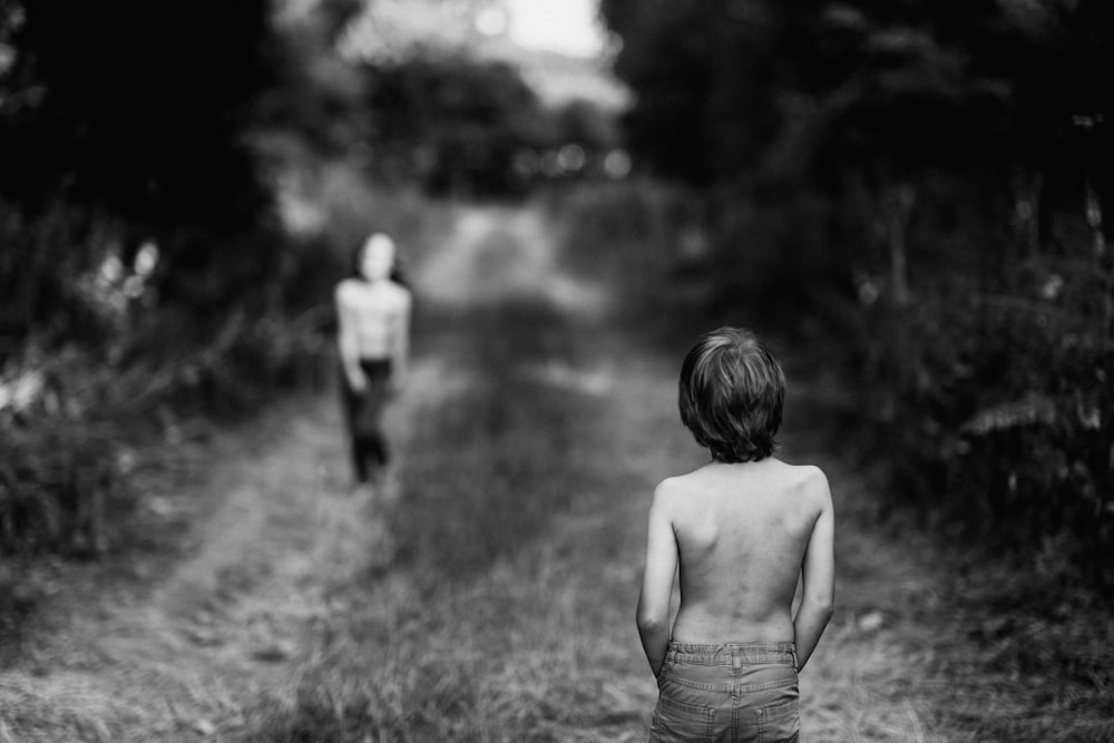 grayscale photography of topless boy on pathway facing girl