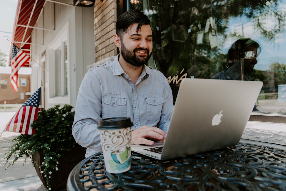 homem na camisa vestido jeans cinza sorrindo ao usar o MacBook Pro