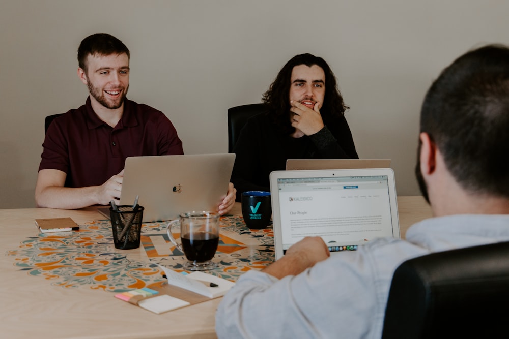 Drei Personen sitzen vor einem Tisch mit Laptops