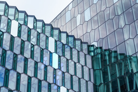 Glass window facade consisting of numerous hexagonal glass panels arranged in a geometric pattern, reflecting the sky and surroundings. Some glass panels are tinted blue and green, adding a variation in color.