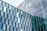 Glass window facade consisting of numerous hexagonal glass panels arranged in a geometric pattern, reflecting the sky and surroundings. Some glass panels are tinted blue and green, adding a variation in color.