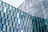 Glass window facade consisting of numerous hexagonal glass panels arranged in a geometric pattern, reflecting the sky and surroundings. Some glass panels are tinted blue and green, adding a variation in color.