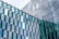 Glass window facade consisting of numerous hexagonal glass panels arranged in a geometric pattern, reflecting the sky and surroundings. Some glass panels are tinted blue and green, adding a variation in color.