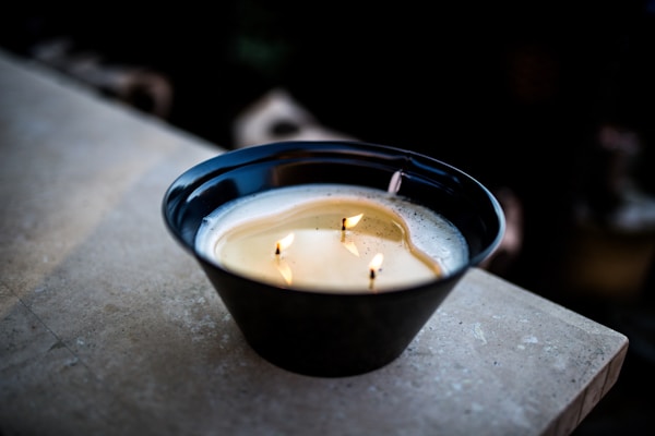 Elegant soy wax candle glowing softly in a black and gold holder on a marble surface.
