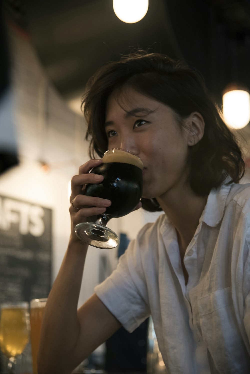 Selektive Fokusfotografie einer Frau, die aus kurzstieligem Glas trinkt