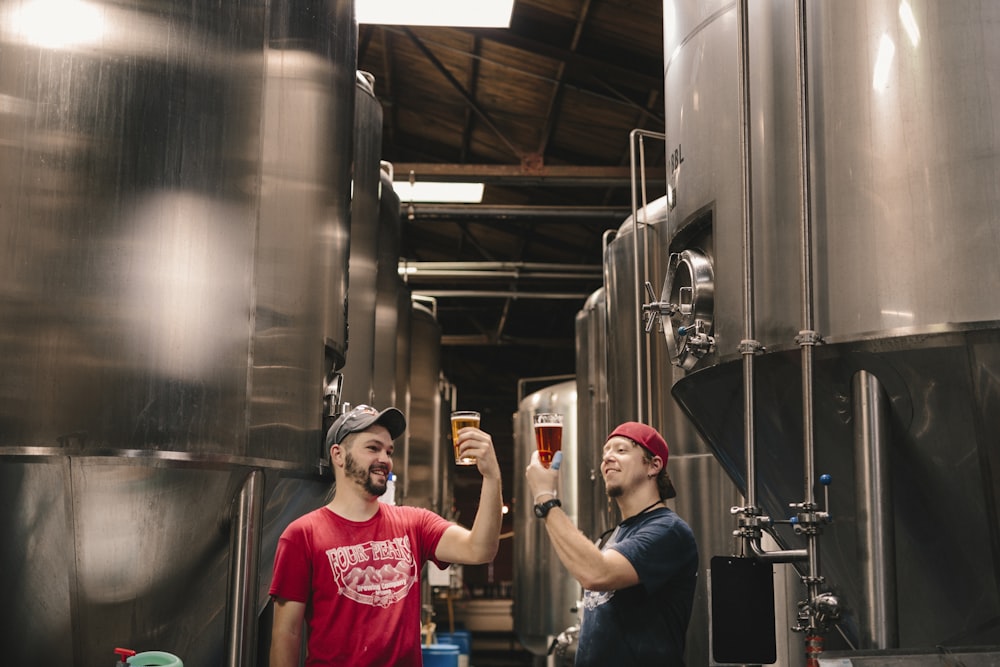 Zwei Männer probieren Bier in der Nähe von zylindrischen Tanks