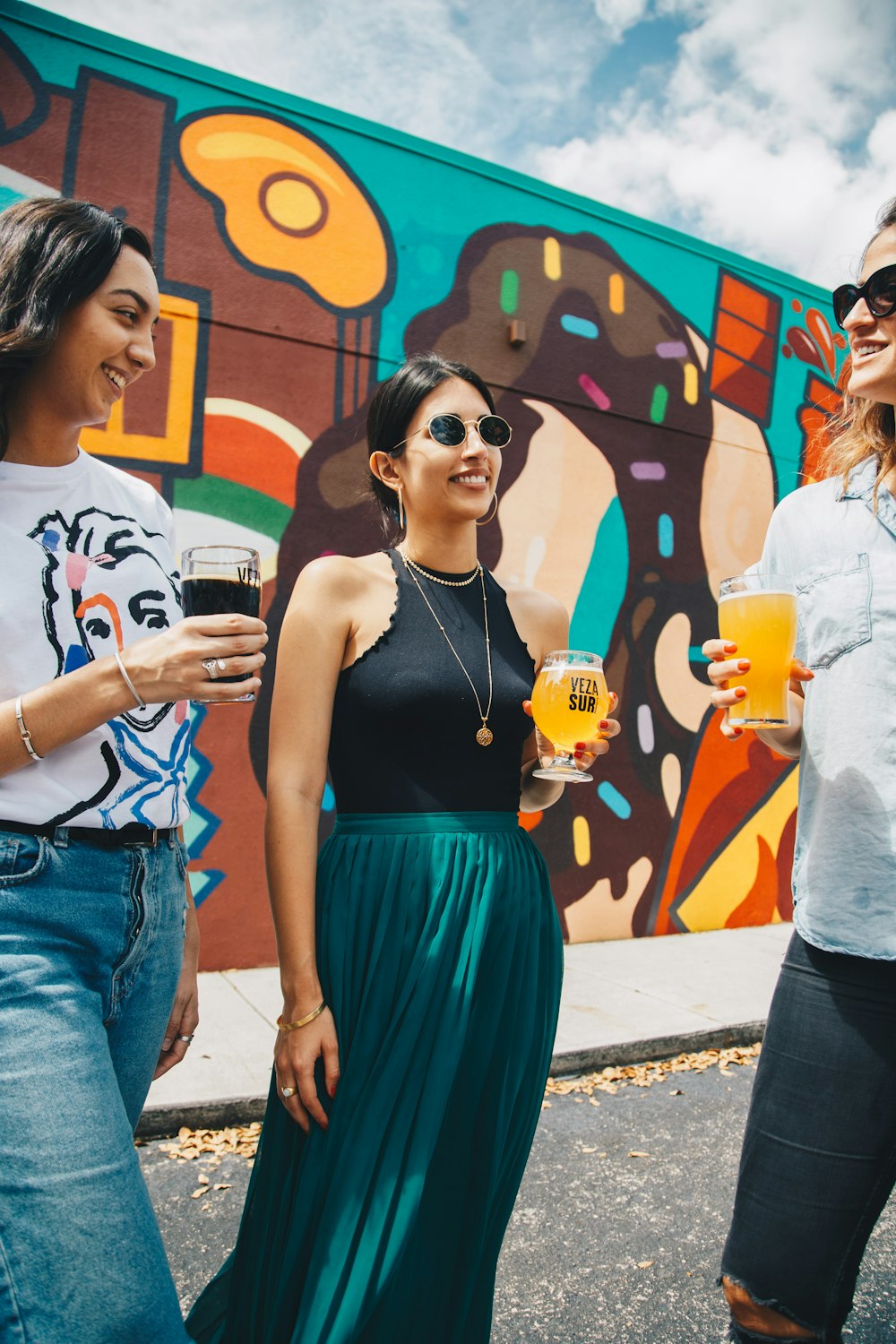 Tres mujeres tomando una copa de pie frente a un grafiti en la pared