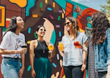 four women holding drinks while laughing together during daytime
