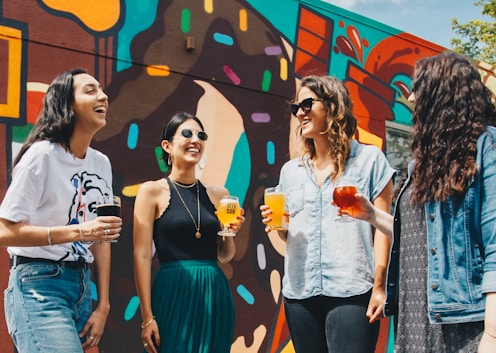 four women holding drinks while laughing together during daytime onlyfans