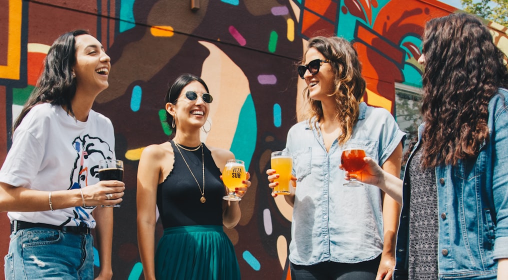 four women holding drinks while laughing together during daytime