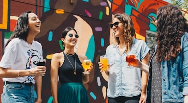 four women holding drinks while laughing together during daytime