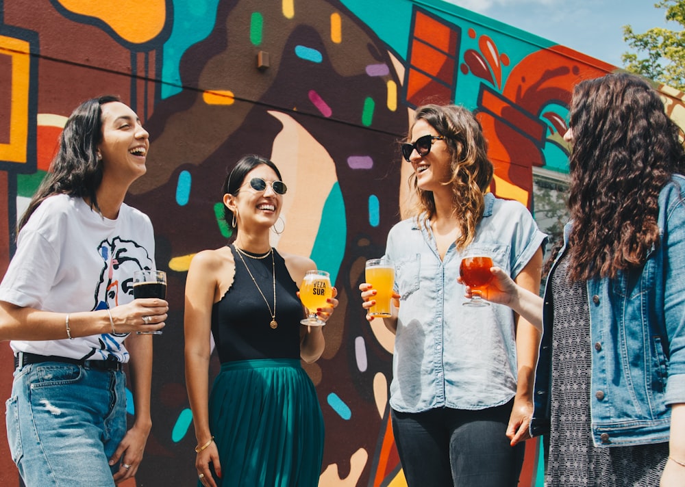 Vier Frauen halten Drinks in der Hand, während sie tagsüber zusammen lachen