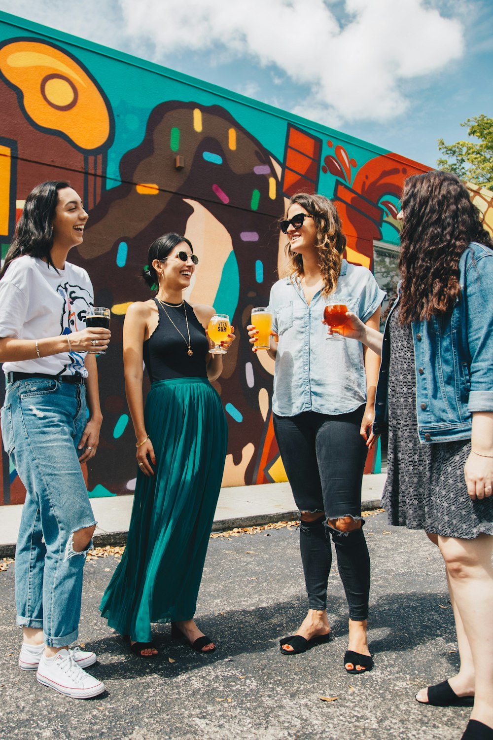 four women standing on paved road holding glass of cocktails