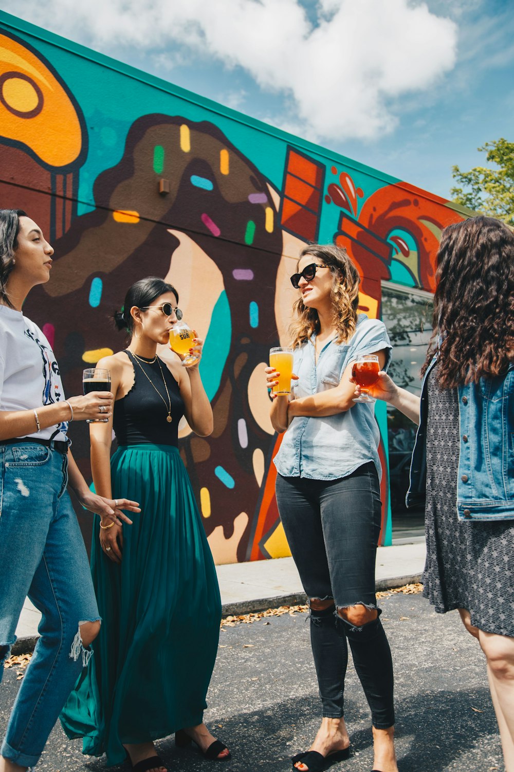 Quatre femmes tenant des boissons aux fruits debout près d’un mur multicolore