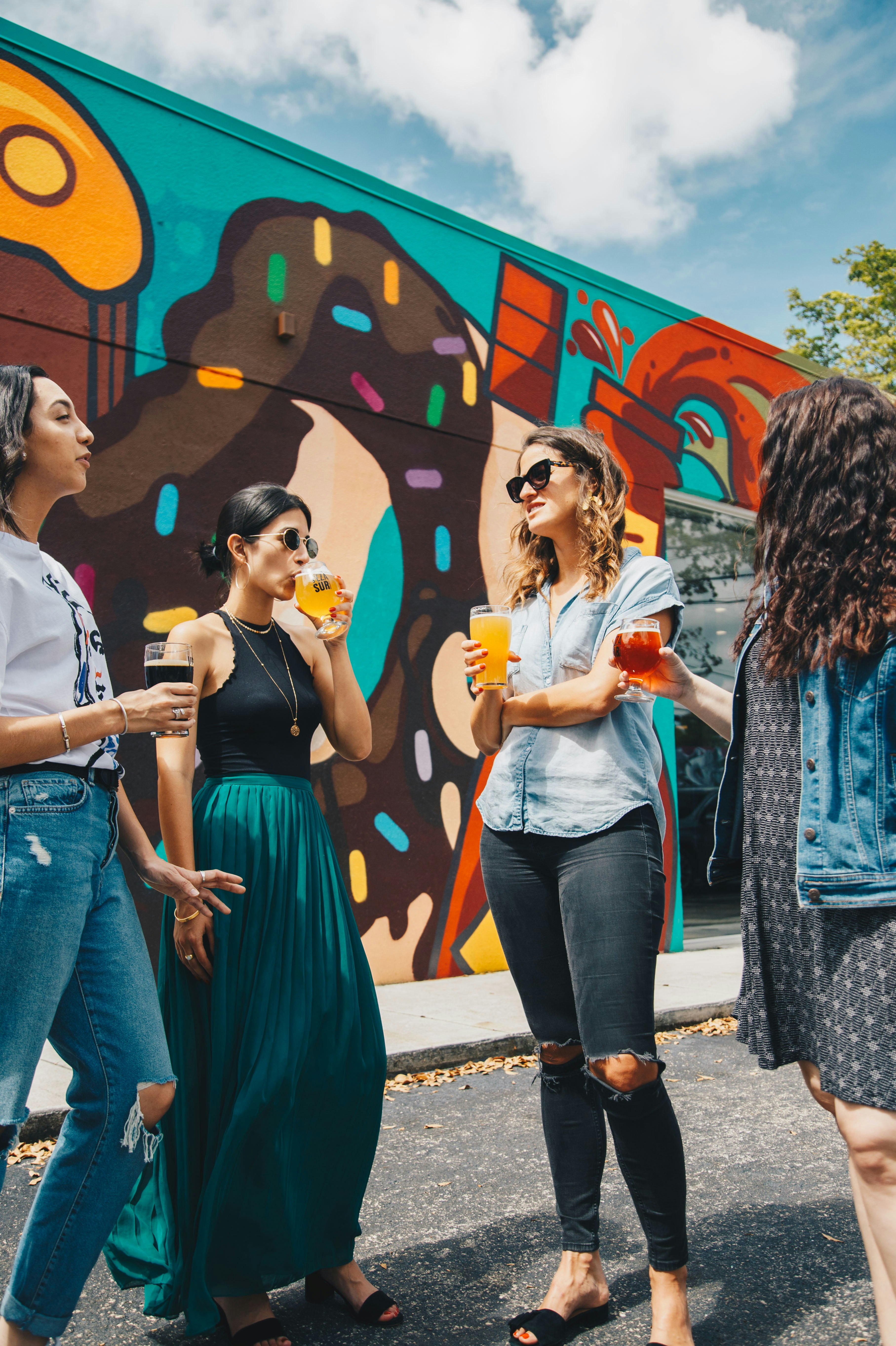 four women holding fruit drinks standing near multicolored wall