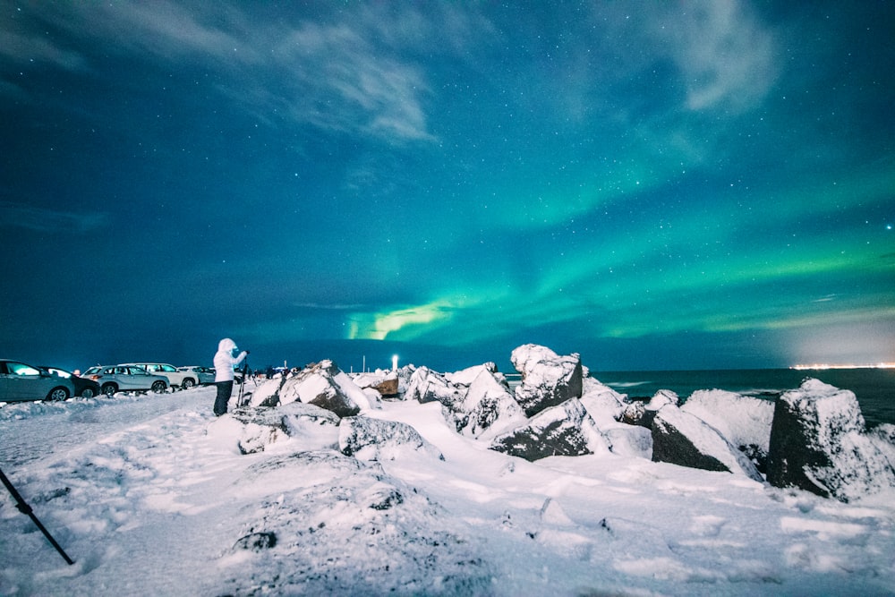 person standing on snowy ground under aurora lights