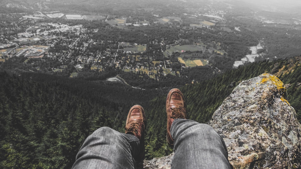 Person, die auf einer Felsformation sitzt, während sie unter das Dorf schaut