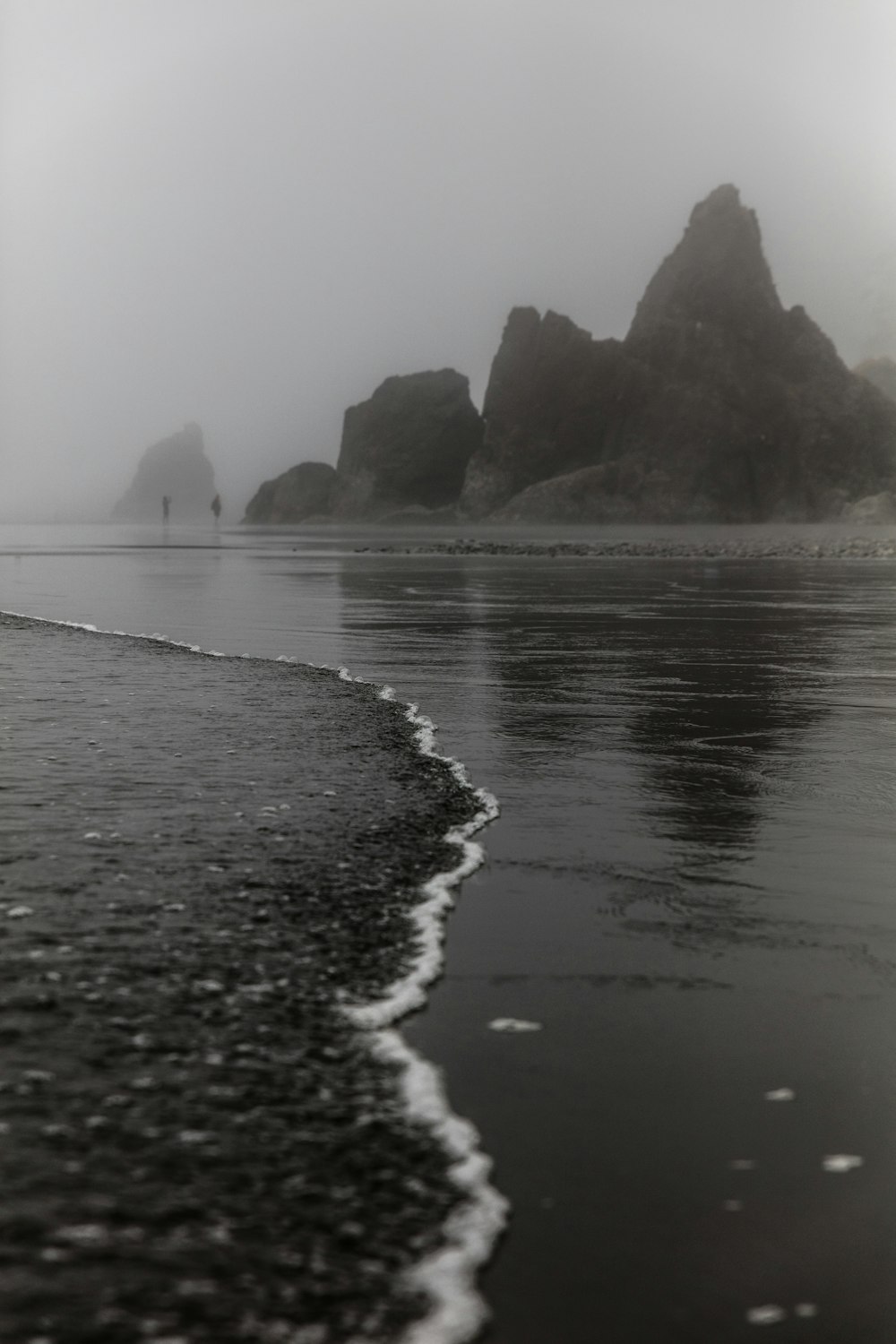 grayscale photography of two person standing in front of rock formation