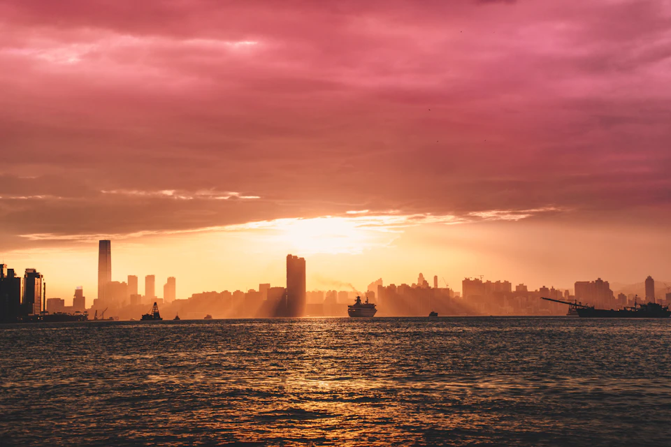 Vibrant city skyline at sunset with warm glow over the waterfront and boats