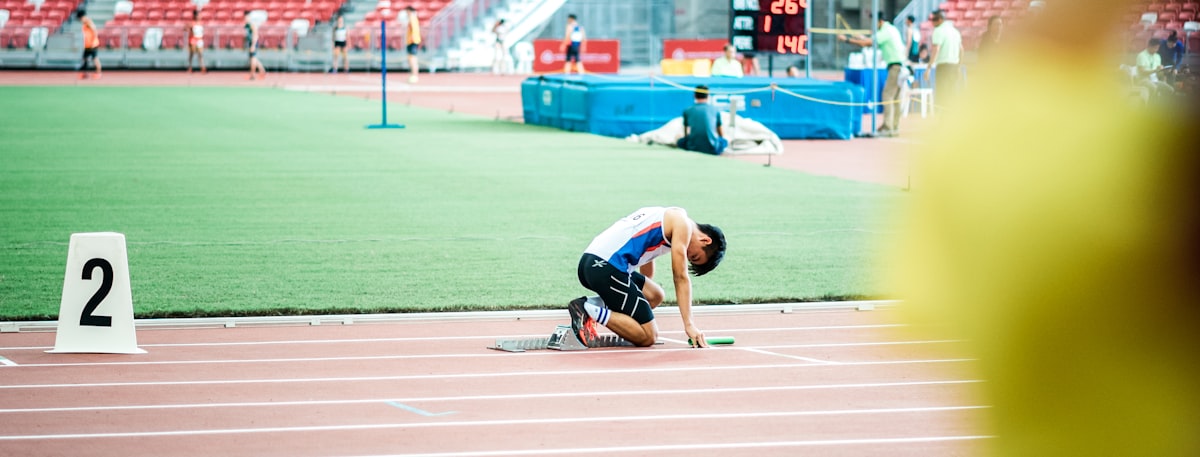 Sprinter in starting position on a track, low and focused before explosive effort.