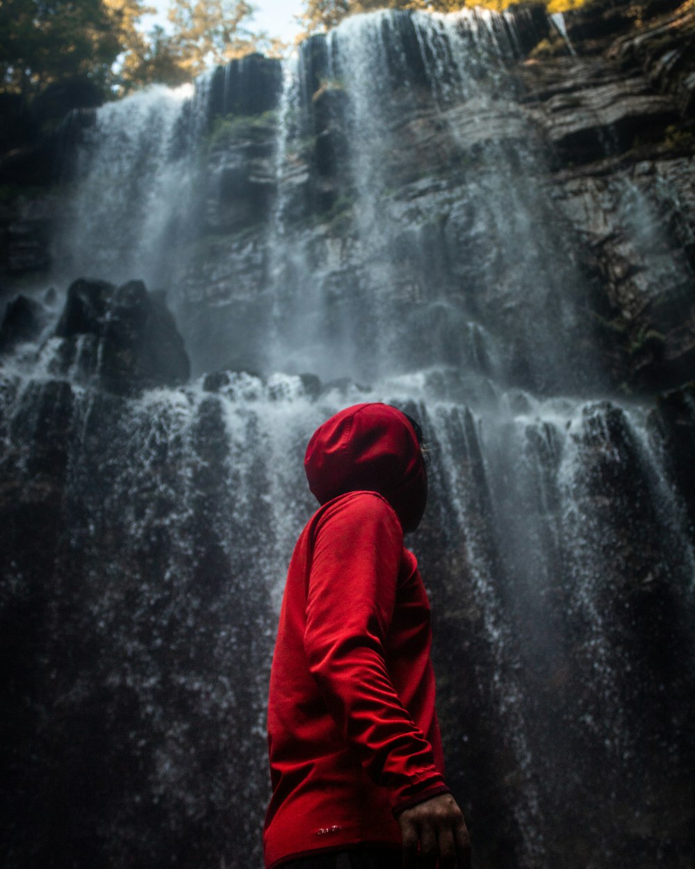フード付きのジャケットを着た男が滝の前に立つ