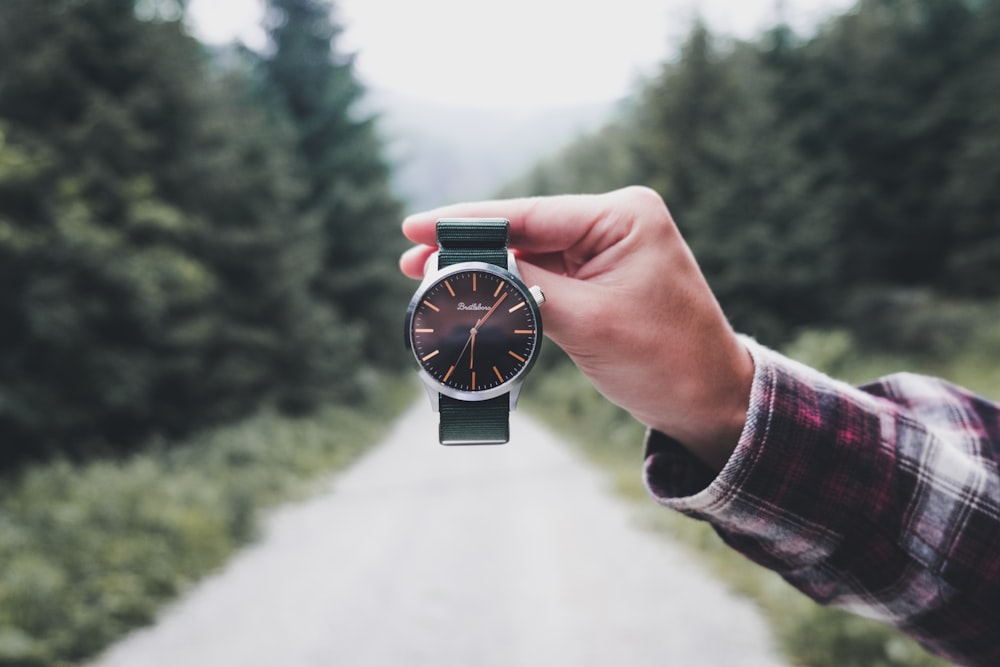 person holding round black analog watch