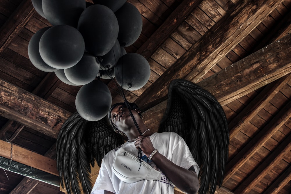 man wearing white shirt holding balloons with wings