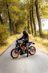 man riding black and orange motorcycle beside trees