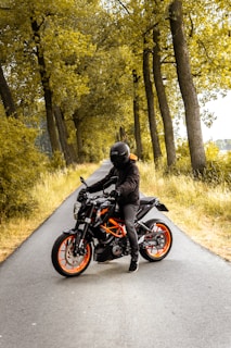 man riding black and orange motorcycle beside trees