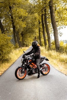 man riding black and orange motorcycle beside trees