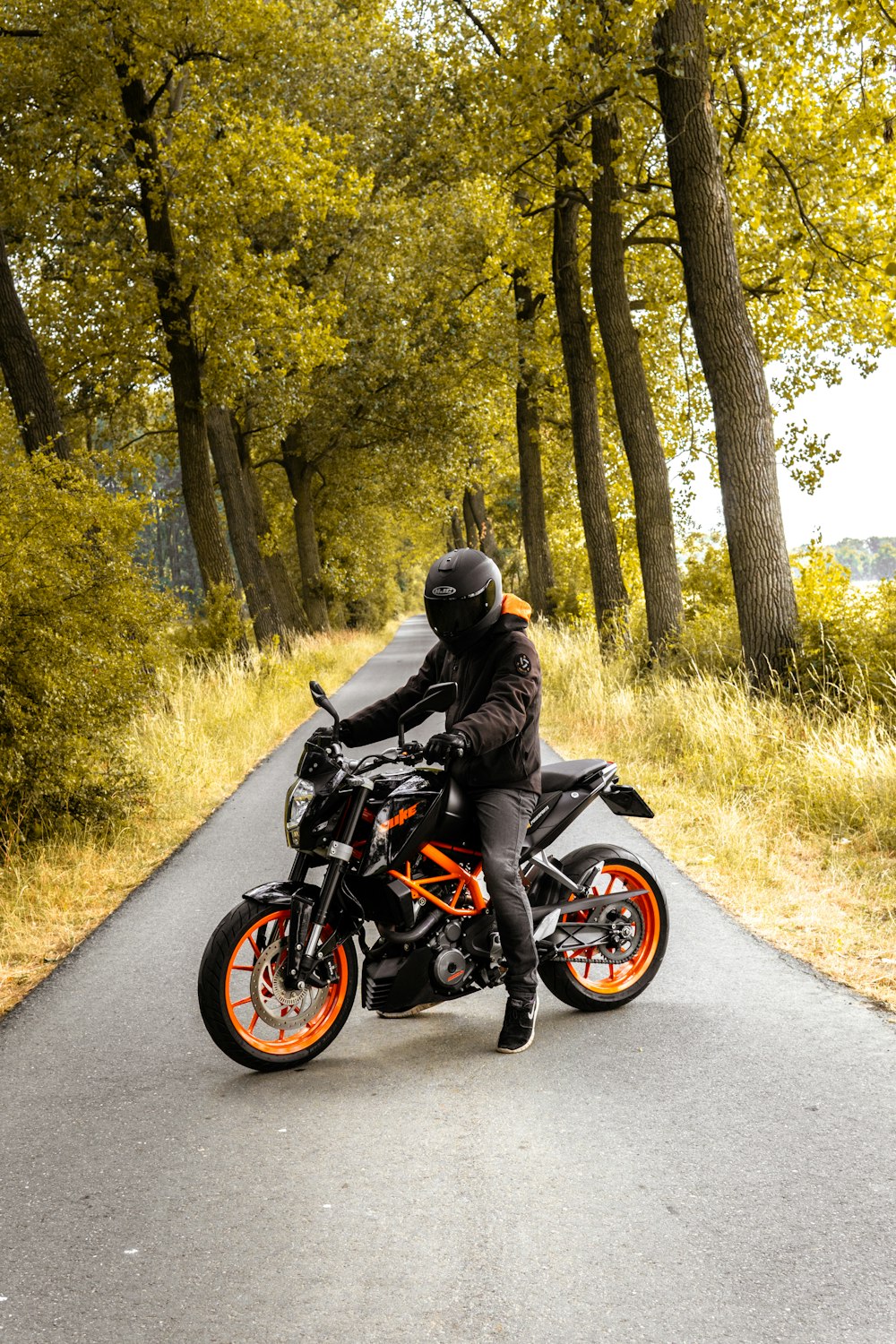 homme conduisant une moto noire et orange à côté d’arbres