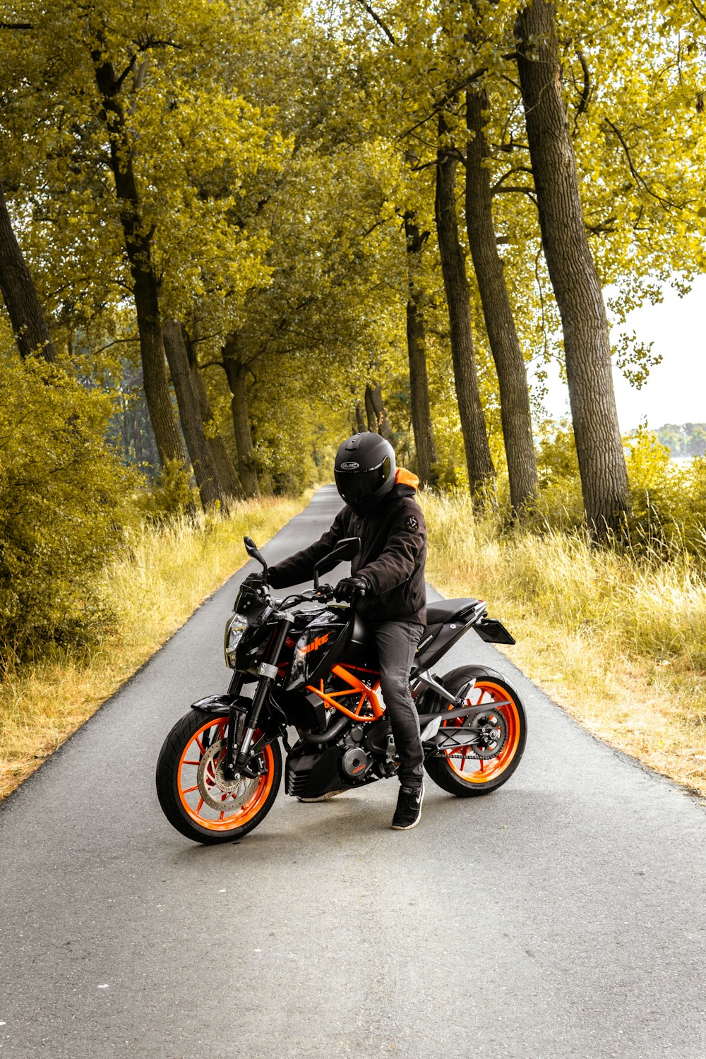 Hombre montando motocicleta negra y naranja al lado de los árboles