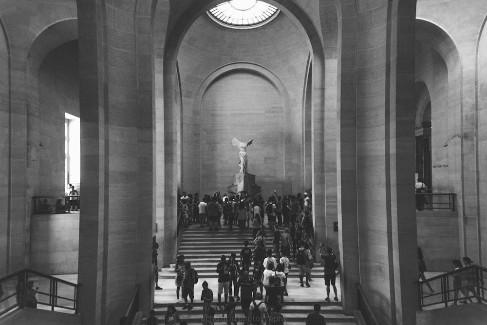 grayscale photo of people walking up the stairs inside building