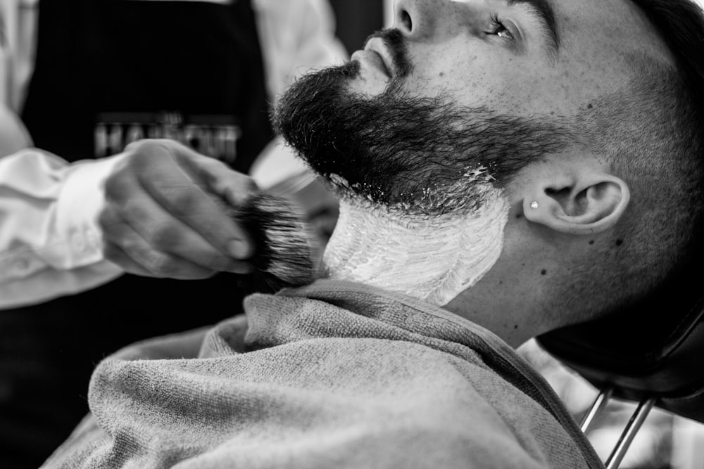 grayscale photo of man shaving his beard