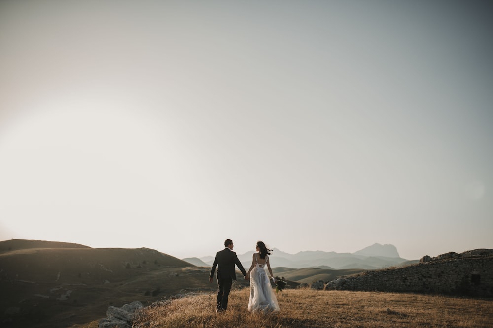 a bride and groom walking on a hill