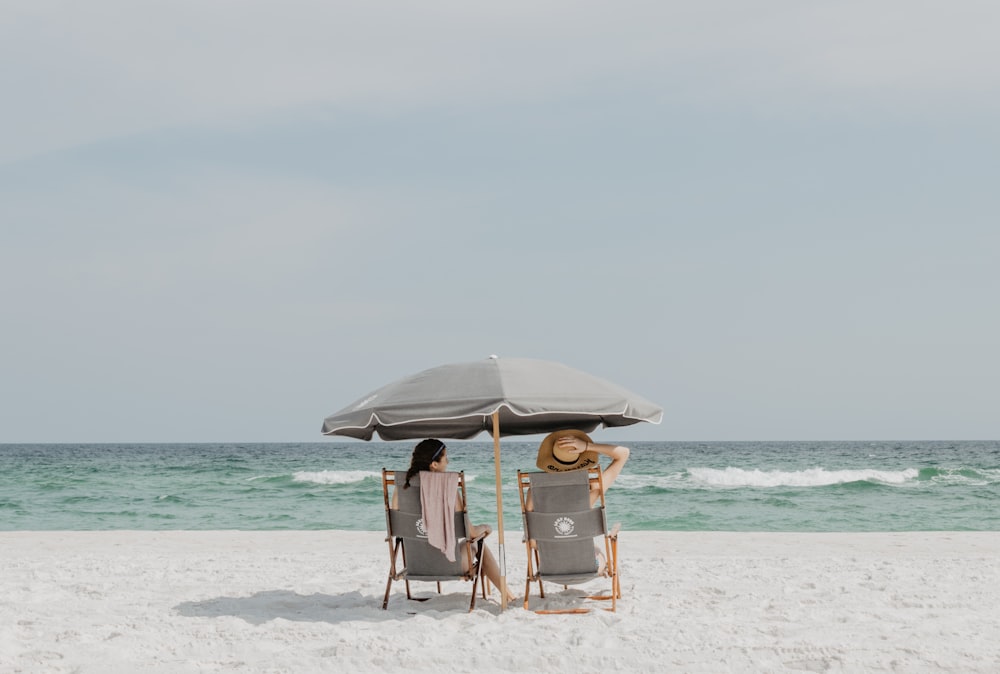 two people under beach umbrella near shoreline