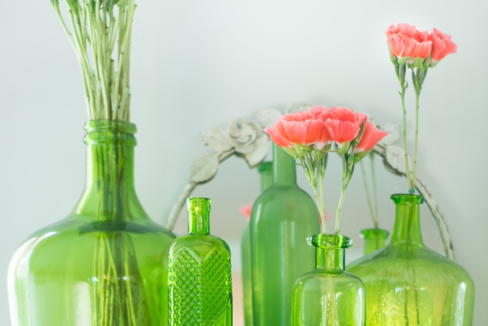 Grüne Grasflaschen mit rosa Blumen neben weißer Wand