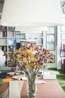 red and yellow petaled flowers in clear glass vase on top of wooden table