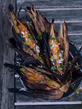 Charred corn on the cob is topped with crumbled cheese and garnished with fresh herbs, set against a rustic wooden background.
