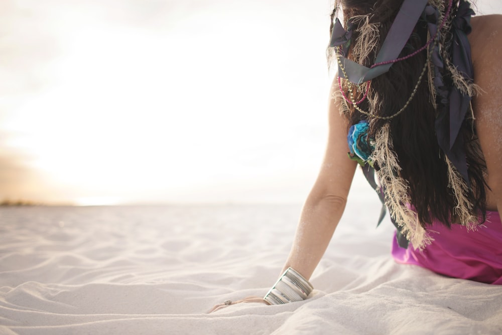 a woman in a pink dress sitting on the sand