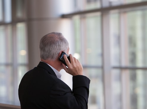 man holding black smartphone in front of a windowpane