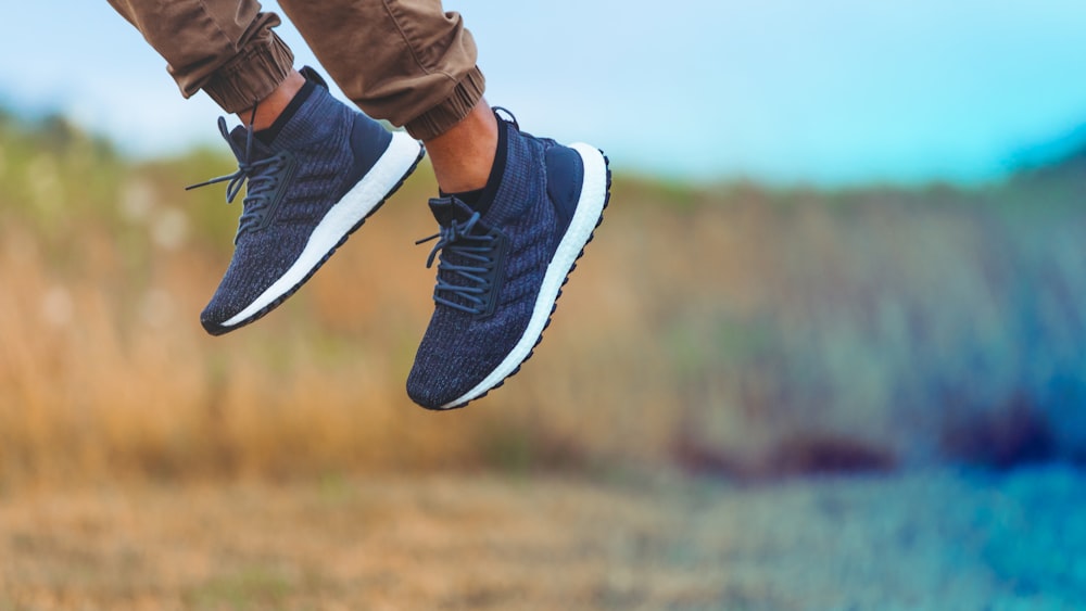 man wearing pair of blue-and-white adidas lace-up low-top sneaker leaping above ground at daytime