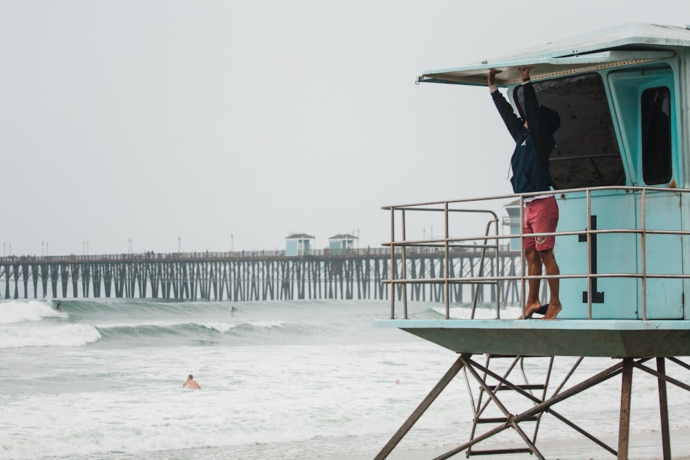 men's black pullover hoodie and red shorts reaching white metal frame beside sea during daytime