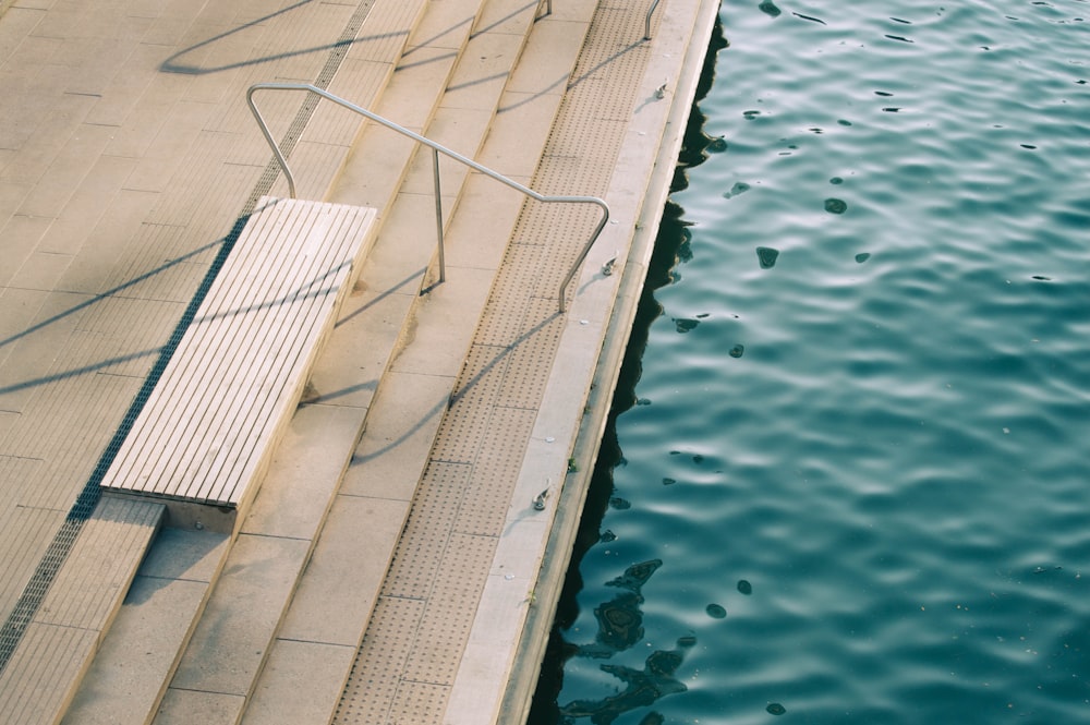 brown concrete stair with white metal railing near body of water during daytime