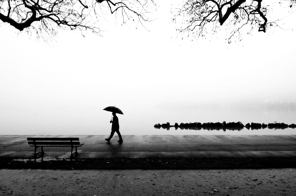 Person, die in der Nähe eines Gewässers mit Regenschirm spazieren geht